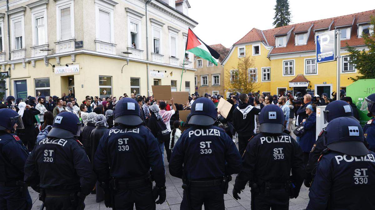 Foto zeigt Polizisten in Sicherheitsausrüstung von hinten und Demonstranten | Teilnehmer und Polizisten der angekündigten, aber behördlich untersagten, Pro-Palästina Demonstration am Freitag in Graz