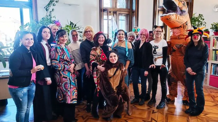 Gruppenbild mit Magierin: Bürgermeisterin Elke Kahr (oder Elke Krah) hat ihr Team im Rathaus um sich versammelt. Sie selbst geht als Magierin mit Rabe auf der Schulter, ihr zu Seite steht Robert Krotzer mit blonder Langhaarperücke. Im Hintergrund blitzt Manfred Eber mit überdimensionierter Peace-Brille hervor. Die meiste Aufmerksamkeit zieht aber der Riesen-Dino auf sich: Mitarbeiter Clemens Fontaine.