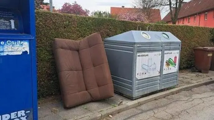 Eine alte Couch lehnt an einer Mülltonne