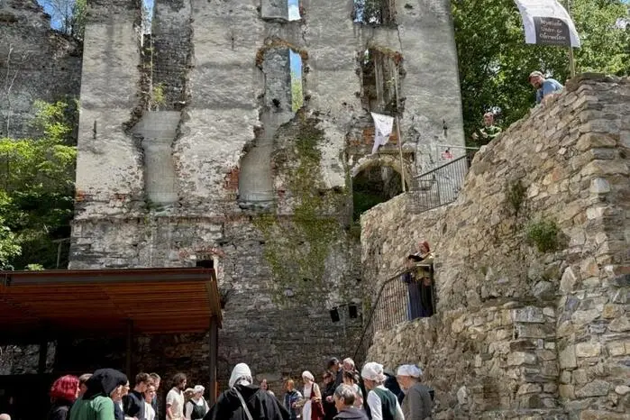 Ein anschauliches, buntes Bild umgeben von mystischem Gemäuer und Besuchern in mittelalterlicher Kleidung. 