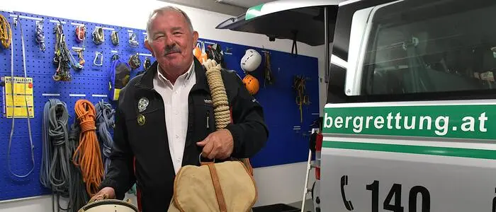Hans Oberhuber mit alter Ausrüstung vor einer Wand mit dem neuen Material