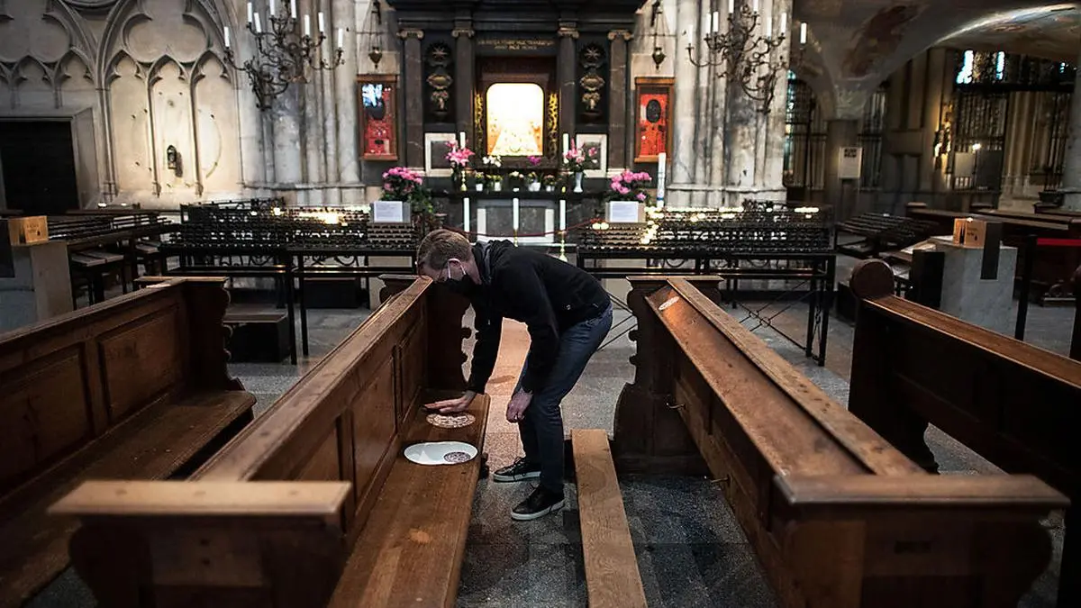 ABD0080_20200430 - KÖLN - DEUTSCHLAND: 30.04.2020, Nordrhein-Westfalen, Köln: Ein Mitarbeiter der Dombauhütte klebt Aufkleber auf Kirchenbänke im Kölner Dom. Die runden Sticker sollen den Platz markieren, auf dem die Gläubigen sich setzen dürfen. In den Kirchen in Nordrhein-Westfalen dürfen von diesem Freitag an wieder Gottesdienste mit Besuchern gefeiert werden. Die Teilnehmerzahl bei den Gottesdiensten ist wegen der Abstandsregeln begrenzt. Foto: Federico Gambarini/dpa +++ dpa-Bildfunk +++. - FOTO: APA/dpa/Federico Gambarini