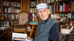 Ein Mann, von der Chemo gezeichnet, sitzt mit einem aufgeschlagenen Buch in seiner Bibliothek  | Emmanuel Longin in seiner Bibliothek in Klagenfurt