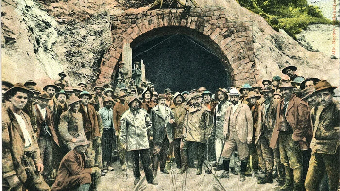 Tausende Arbeiter haben Anfang des 20. Jahrhunderts in Schwerstarbeit einen Tunnel für die Karawankenbahn in den Berg gegraben: 1904 gruppierten sich Ingenieure und Arbeiter vor dem Eingang auf der Kärntner Nordseite, blickten stolz und handkoloriert in die Kamera. Diese Karte gehört zu einer Serie von Postkarten, die den Bau der Karawankenbahn dokumentieren und sich in der Sammlung der Universitätsbibliothek Klagenfurt finden.