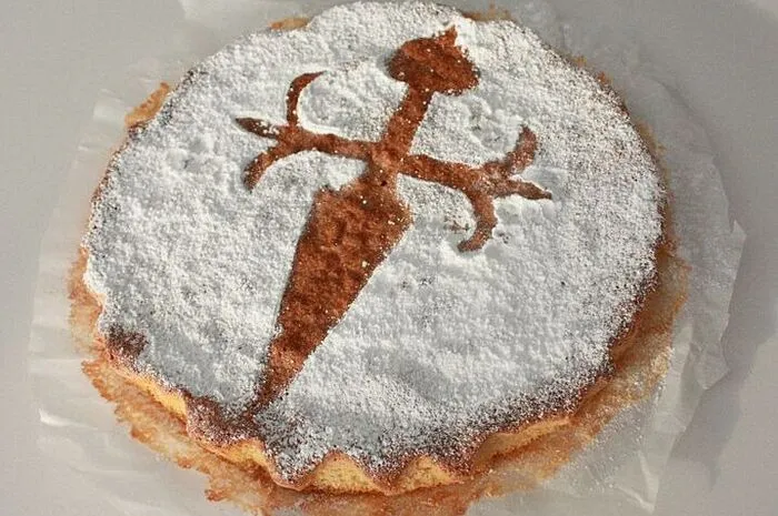 Dieser Mandel-Kuchen aus Galizien wurde erstmals 1577 erwähnt. Charakteristisch für die Tarta ist das Kreuz des Santiago-Ordens auf der Kuchendecke. Das heutige Rezept wurde seit 1828 nicht verändert: Die Hauptzutaten sind neben Zucker und Eiern vor allem Mandeln, wodurch dieTarta ohne Mehl auskommt. Beliebt ist sie heute im ganzen Land, bei Einheimischen wie Touristen. Nach einem Stück Torta de Santiago mit 377 Kalorien laufen Madrid-Besucher rund 108 Minuten, um die verspeisten Kalorien zu kompensieren. Wer als Pilger auf dem Jakobsweg nach Santiago unterwegs ist, kann wohl einige Stücke pro Tag verputzen.
