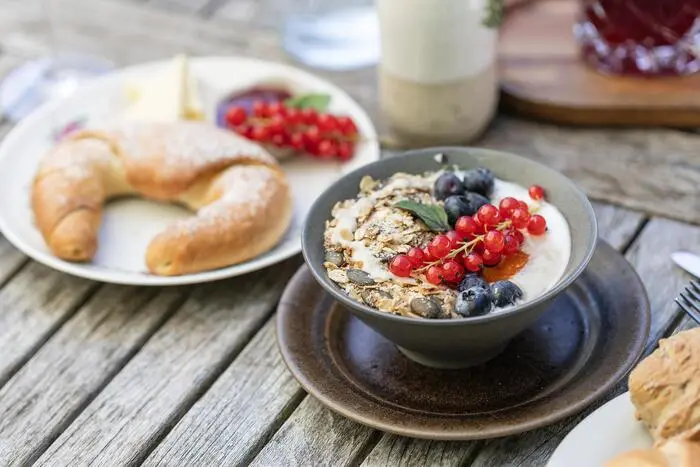Müsli mit Ribiseln und Heidelbeeren, im Hintergrund ein Kipferl. 