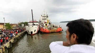 epa04554926 An Indonesian man looks at Indonesian national search and rescue agency's (BASARNAS) crew lift up the ruins of AirAsia QZ8501 aircraft tail from the Crest Onyx ship, after hoisted from the Java Sea during their recovery mission at Panglima Utar Kumai Harbour in Kumai, Central Borneo, Indonesia, 11 January 2015. The search party working to recover wreckage of a crashed AirAsia flight hoisted the plane's tail section out of the Java Sea on 10 January. EPA/BAGUS INDAHONO
