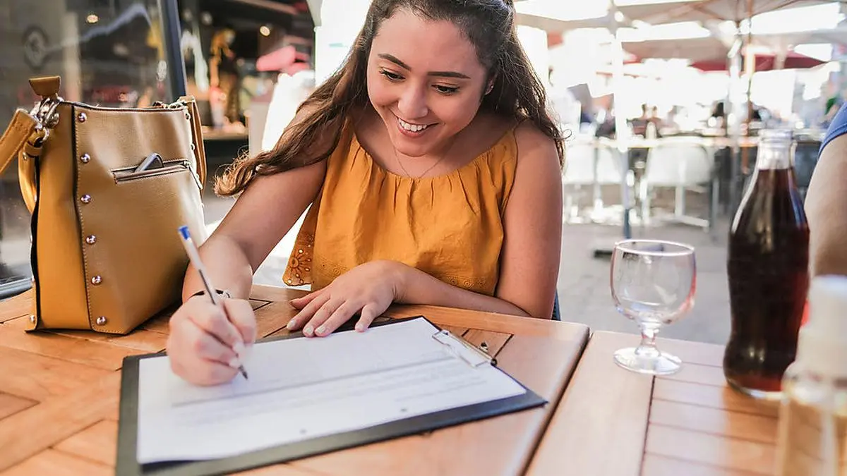 Happy young woman fills out contact person list in a restaurant - Coronavirus lifestyle
