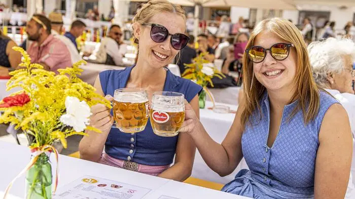 Zwei Frauen sitzen in Tracht bei einem Fest und prosten sich mit Bier an