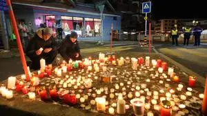 People lay candles near the Le Constellation bar, where a devastating fire left dead and injured during the New Year's celebrations in Crans-Montana, Swiss Alps, Switzerland, Thursday, Jan. 1, 2026. (AP Photo/ Antonio Calanni)