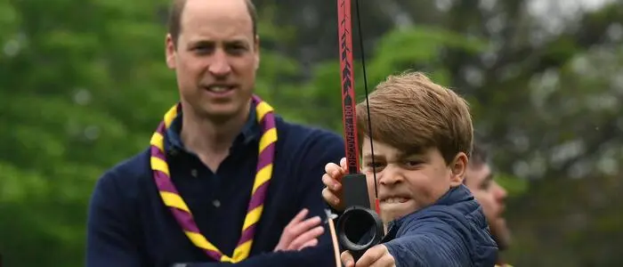 Prinz George mit Pfeil und Bogen, dahinter steht sein Vater Prinz William mit verschränkten Armen