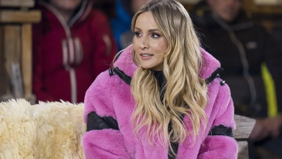 Frau in Pinkem Pelzmantel auf einer Fellbank, dahinter sitzende Skifahrer | Melissa Naschenweng während der ServusTV-Sendung „Sport und Talk aus dem Hangar-7", diesmal auf der Seidlalm in Kitzbühel