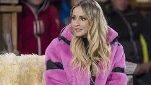 Frau in Pinkem Pelzmantel auf einer Fellbank, dahinter sitzende Skifahrer | Melissa Naschenweng während der ServusTV-Sendung „Sport und Talk aus dem Hangar-7", diesmal auf der Seidlalm in Kitzbühel