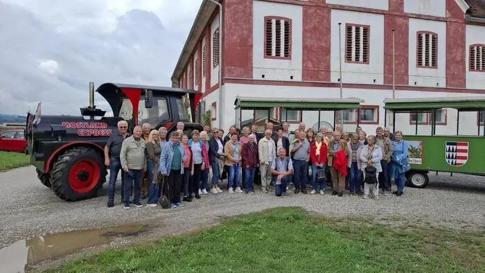 Eine große Gruppe Senioren steht neben einem Traktor auf einem Bauernhof