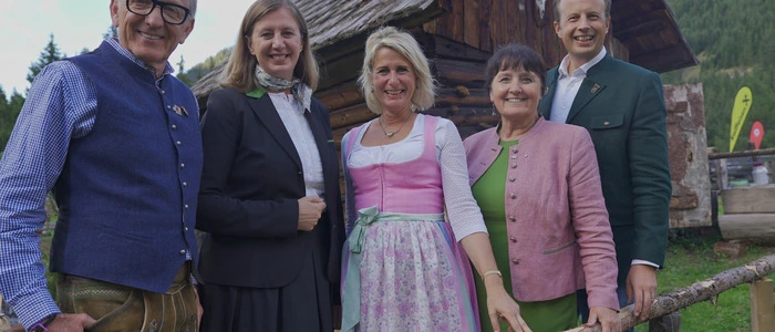Drei Frauen und zwei Männer stehen in Tracht gekleidet vor einer Almhütte.