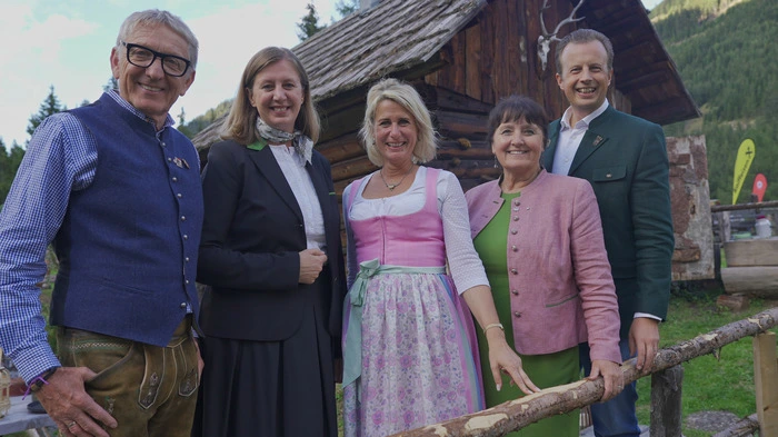 Drei Frauen und zwei Männer stehen in Tracht gekleidet vor einer Almhütte.