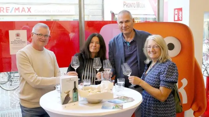 Zwei Männer und zwei Frauen stehen an einem Tisch und halten ein Glas Wein in den Händen.