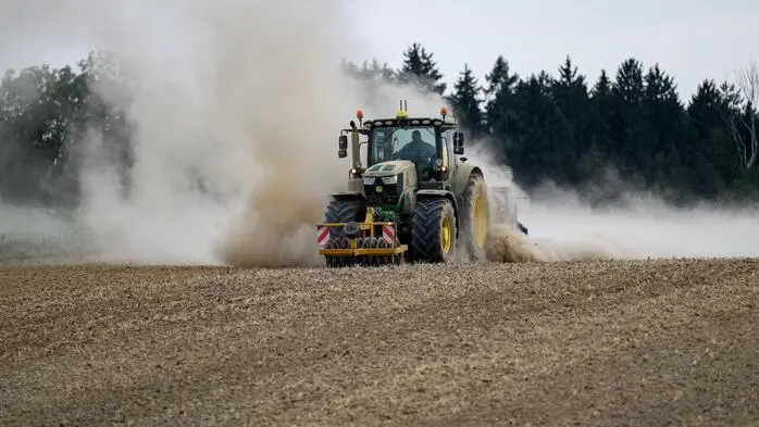 Ein Traktor mit landwirtschaftlichen Anbaugeräten und Sämaschine bearbeitet einen trockenen Acker