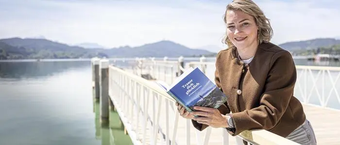 Eine junge Frau steht auf einem Steg und hält ein Buch in der Hand