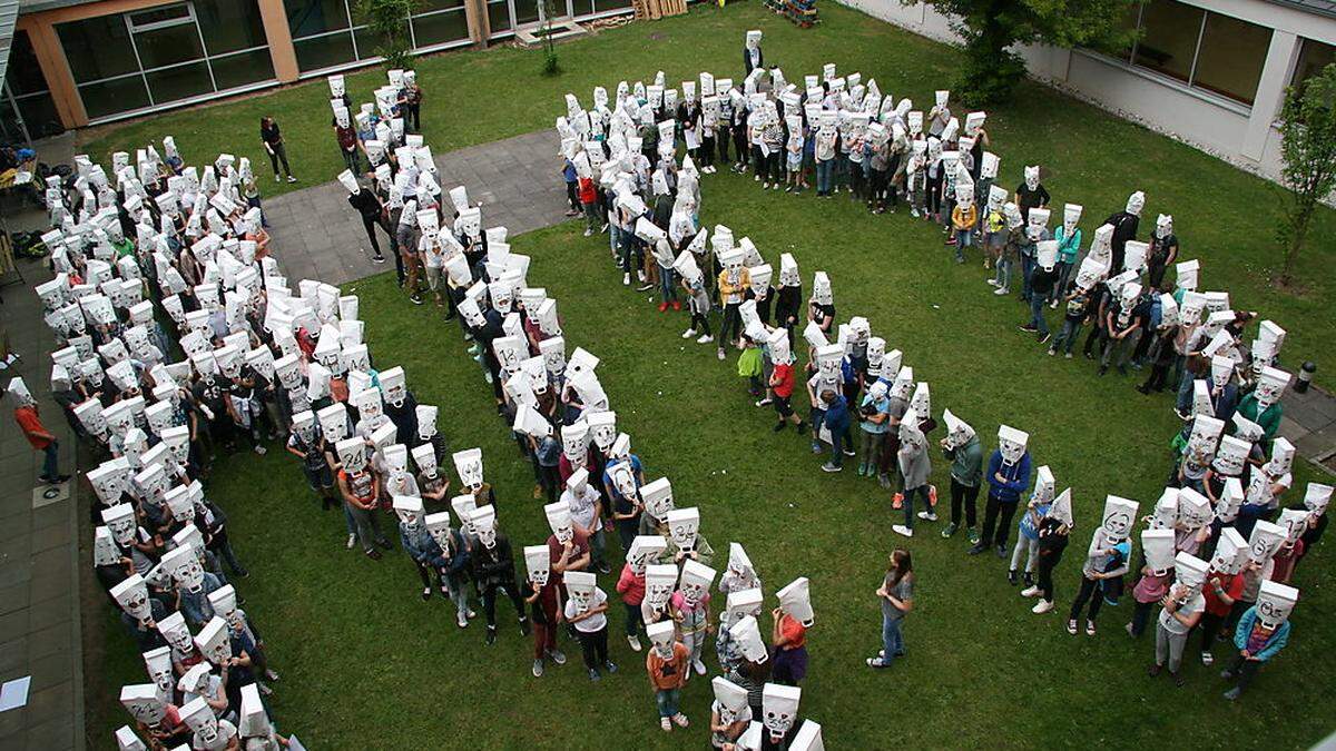 Mit Papiersäcken mit aufgezeichneten Nummern über ihren Köpfen, machten die Schüler auf ihre Situation im Schulinnenhof aufmerksam