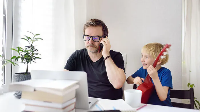 Man working from home with laptop during quarantine. Home office and parenthood at same time. Exhausted parent with hyperactive child.