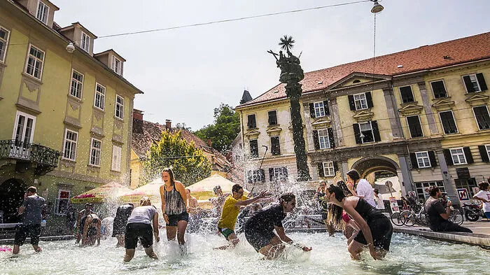 Beste Abkühlung nach einem schweißtreibenden Aufstieg durch die Sporgasse: der Brunnen am Karmeliterplatz. Das Baden ist zwar untersagt, aber zumindest die Füße können schon einmal ganz kurz eingetaucht werden. Oder man macht einen Flashmob, wie damals 2015.