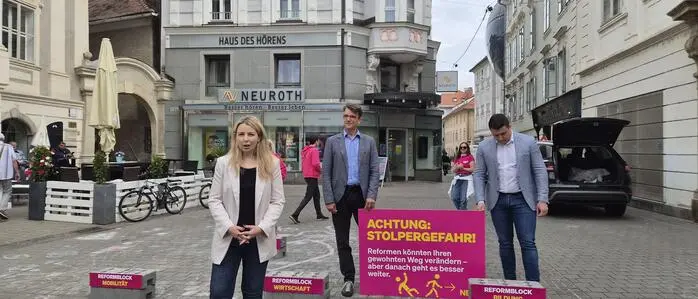 Verena Garber mit weißem Sakko, dunklem Leiberl und Hose sowie hellen Schuhen, steht beim Wahlkampfauftakt an vorderster Stelle; im Hintergrund Philipp Poinntner (Mann mit Sakko und blauem Hemd) und Alexis Pascuttini (Blick nach unten, hellblaues Sakko, weißes Hemd)