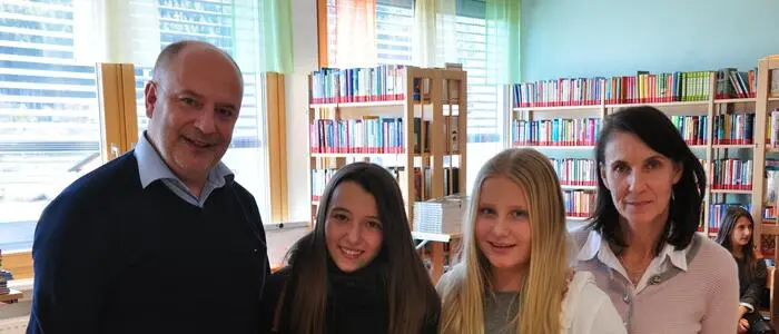 Ein erwachsener Mann und eine erwachsene Frau stehen mit zwei Schülerinnen in einer Bibliothek