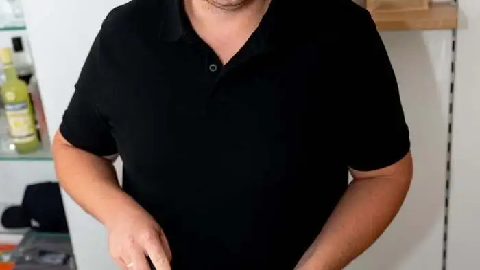 Ein Mann mit schwarzem Hemd schneidet eine Torte auf
