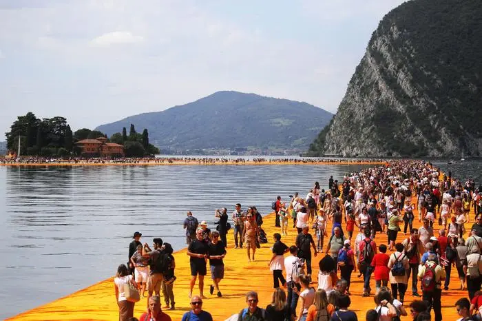 (FILES) In this file photo taken on June 18, 2016 people walk on the monumental installation entitled 'The Floating Piers' created by artist Christo Vladimirov Javacheff on Iseo Lake, in northern Italy. - The artist known as Christo, who made his name transforming landmarks such as Germany's Reichstag by covering them with reams of cloth, died on May 31, 2020 aged 84, his official Facebook page announced. Christo Vladimirov Javacheff died of natural causes at his home in New York City, the statement said. The Bulgarian-born artist worked in collaboration with his wife of 51 years Jeanne-Claude until her death in 2009. (Photo by MARCO BERTORELLO / AFP) / RESTRICTED TO EDITORIAL USE - MANDATORY MENTION OF THE ARTIST UPON PUBLICATION - TO ILLUSTRATE THE EVENT AS SPECIFIED IN THE CAPTION