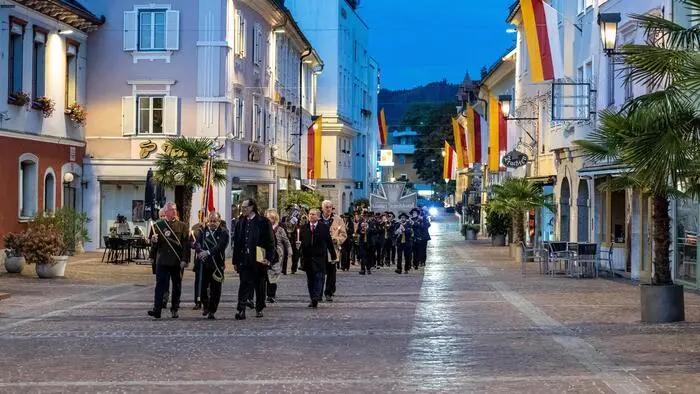 Männer in traditionellen Kärntner Gewändern marschieren durch eine Altstadt bei Abenddämmerung