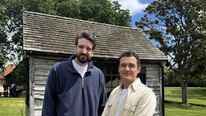 Simon Reinelt und Orlando Bloom vor einer Holzhütte.