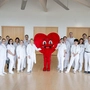 Das Team der Herz-Kreislauf-Rehabilitation in Althofen, alle in weißer Kleidung. In der Mitte sieht man ein Maskottchen in Herzform.