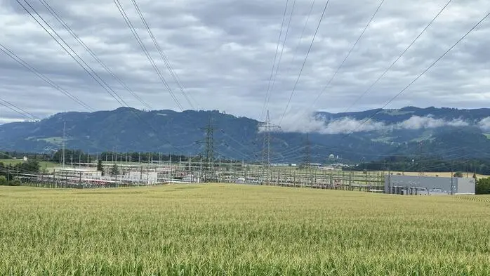 Ein Maisfeld mit dem Umspannwerk Obersielach im Hintergrund. Man sieht Stromleitungen, die zum Umspannwerk führen | Beim Umspannwerk Obersielach in der Gemeinde Völkermarkt soll die Trasse enden