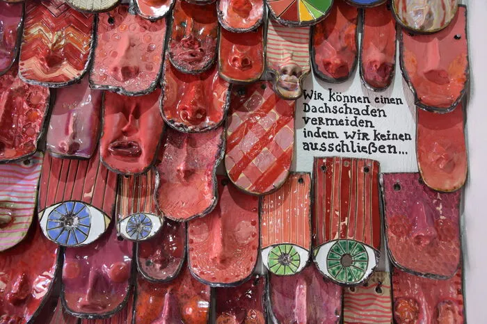 Rote und rosafarbene Dachziegel mit Nasen, Mündern und Augen zieren eine Vertiefung in der Wand. "Wenn nur einer fehlt, entsteht ein Dachschaden. Deshalb sollte man besser keinen ausschließen", so Binder.