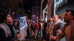 Mehrere Demonstranten mit dem „Palästinensertuch“ Kufiya um den Hals gehängt, stehen vor einer Starbucks-Filiale in Barcelona und bilden davor eine Menschenkette, um Kunden den Zutritt zu verwehren. Eine Frau hält ein Protestschild hoch | Demonstranten riegeln eine Starbucks-Filiale in Barcelona ab
