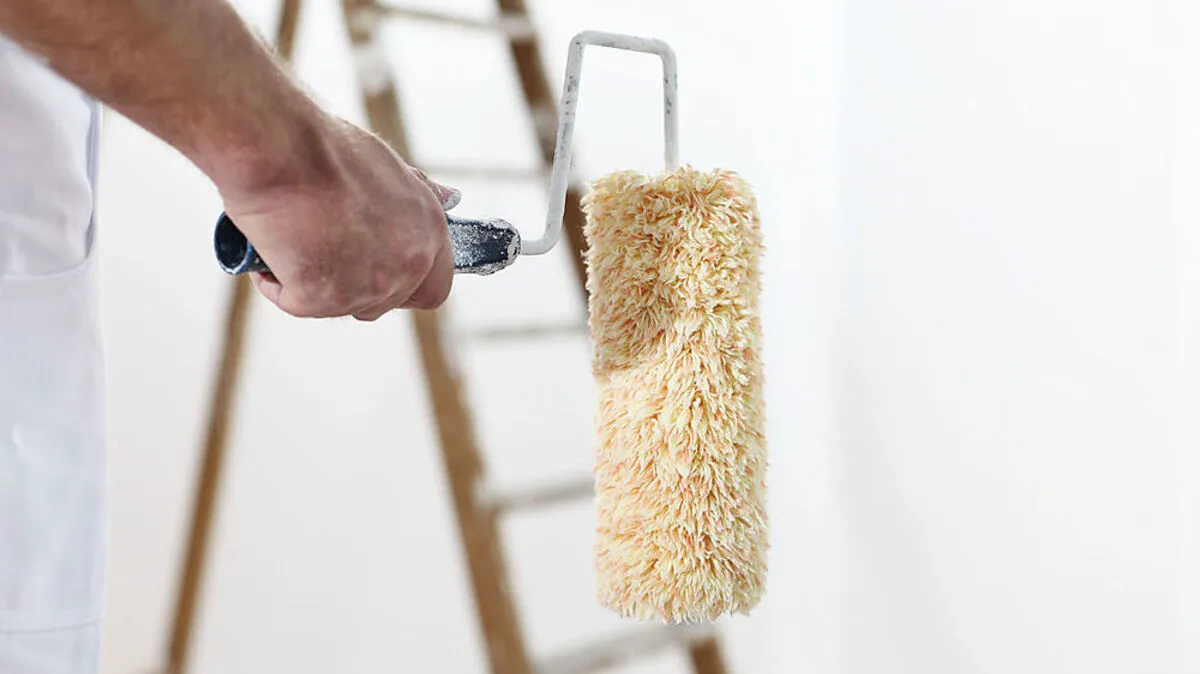 painter man at work with a paint roller and ladder, hand clsose up