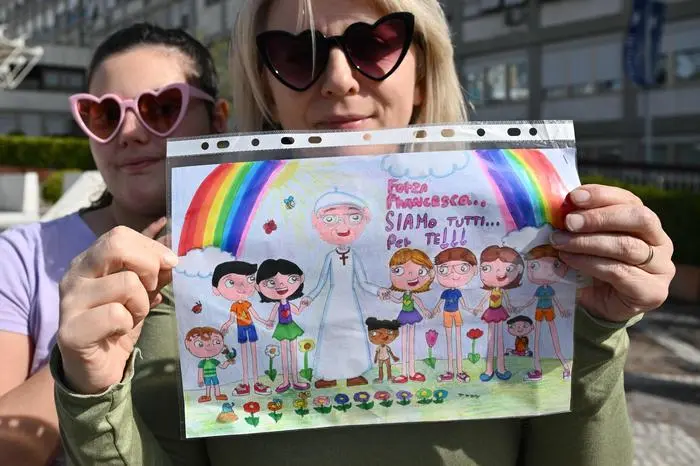 Violetta from Poland and her daugther Maria show a drawing for Pope Francis outside the Gemelli hospital where Pope Francis is hospitalized for pneumonia, in Rome on February 23, 2025. Pope Francis had a quiet night in hospital, the Vatican said on February 23, 2025, the morning after revealing the 88-year-old was in a 