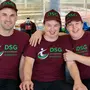 Drei Personen sitzen nebeneinander und tragen die gleiche dunkelrote Uniform mit grüner Schrift und Kappe 