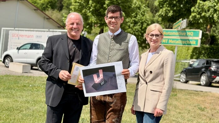 Eine Frau und zwei Männer stehen nebeneinander. Einer der Männer hält ein Bild einer Burg in der Hand