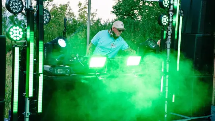 Ein DJ steht an einem Mischpult und ist von grünem Rauch umgeben