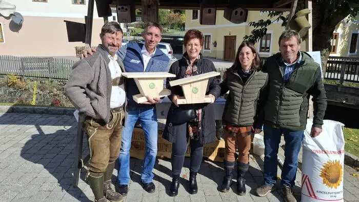 Fünf erwachsene Personen stehen im Freien und zwei von ihnen haben Vogelhäuser in den Händen