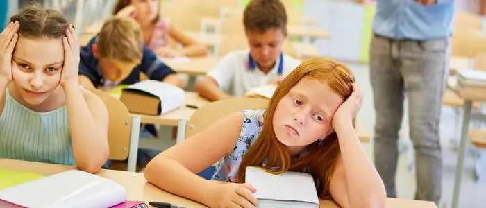 Mehrere Schülerinnen und Schüler sitzen mit erschöpftem Gesichtsausdruck in einem Klassenzimmer