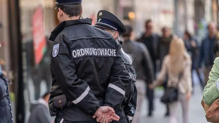 Zwei Ordnungswache-Beamte auf Streife durch Graz; zu sehen ist der Rücken eines Beamten mit der großen Aufschrift „Ordnungswache“