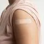 Asian woman shows plaster on her shoulder after being vaccinated against Covid-19. Coronavirus vaccination campaign concept.