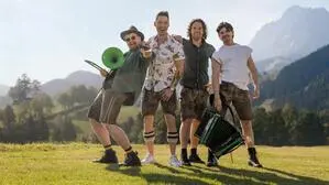 Vier Männer stehen auf einer Wiese und halten Musikinstrumente in ihren Händen.