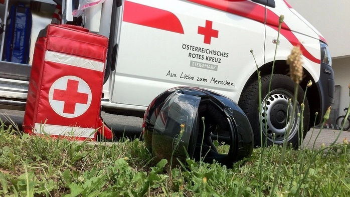 Ein schwarzer Sturzhelm liegt in einer Wiese direkt neben einem Rettungswagen
