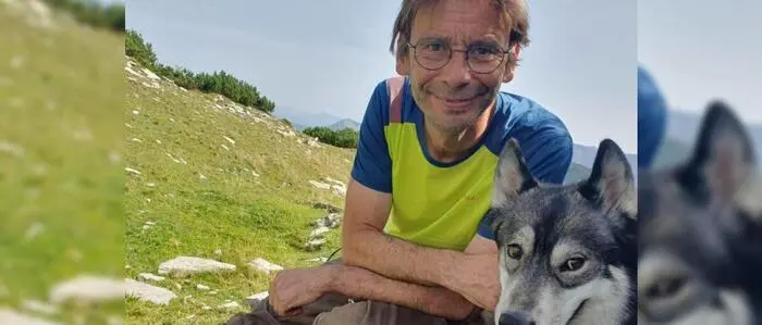 Ein Mann sitzt mit seinem Hund auf einer Almwiese