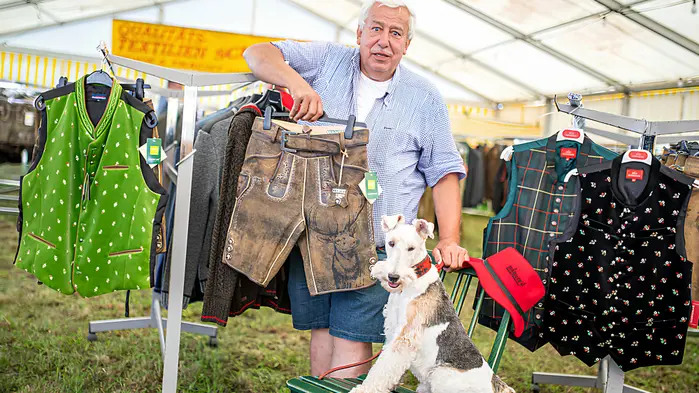 Mann mit weißen Haaren steht vor Trachtenmode, neben ihm ein Hund