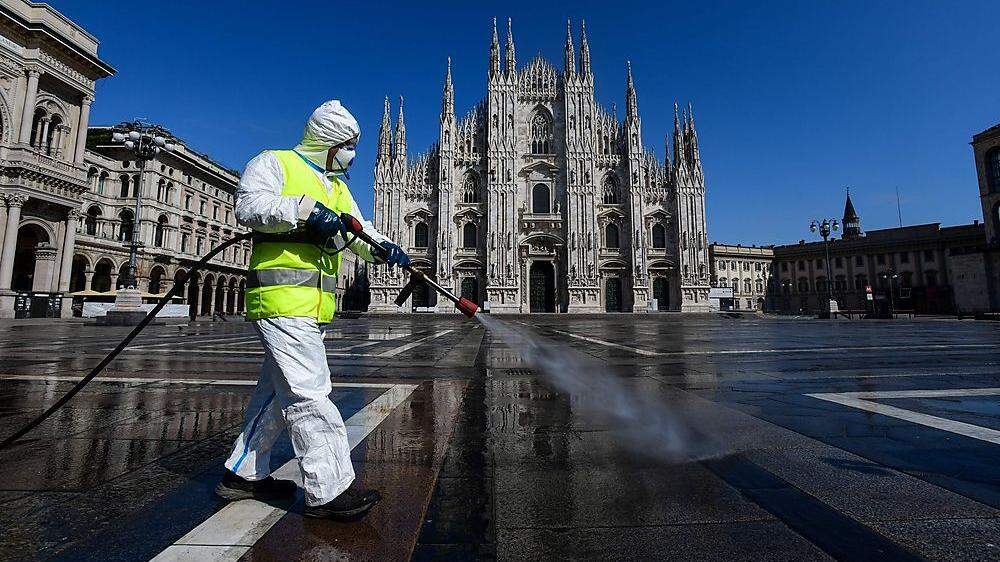 Ein Stadtbeauftragter in Schutzkleidung versprüht Desinfektionsmittel auf Mailands Piazza Duomo